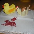 Račka in kokoška iz barvnega papirja na velikonočnem prtičku.
